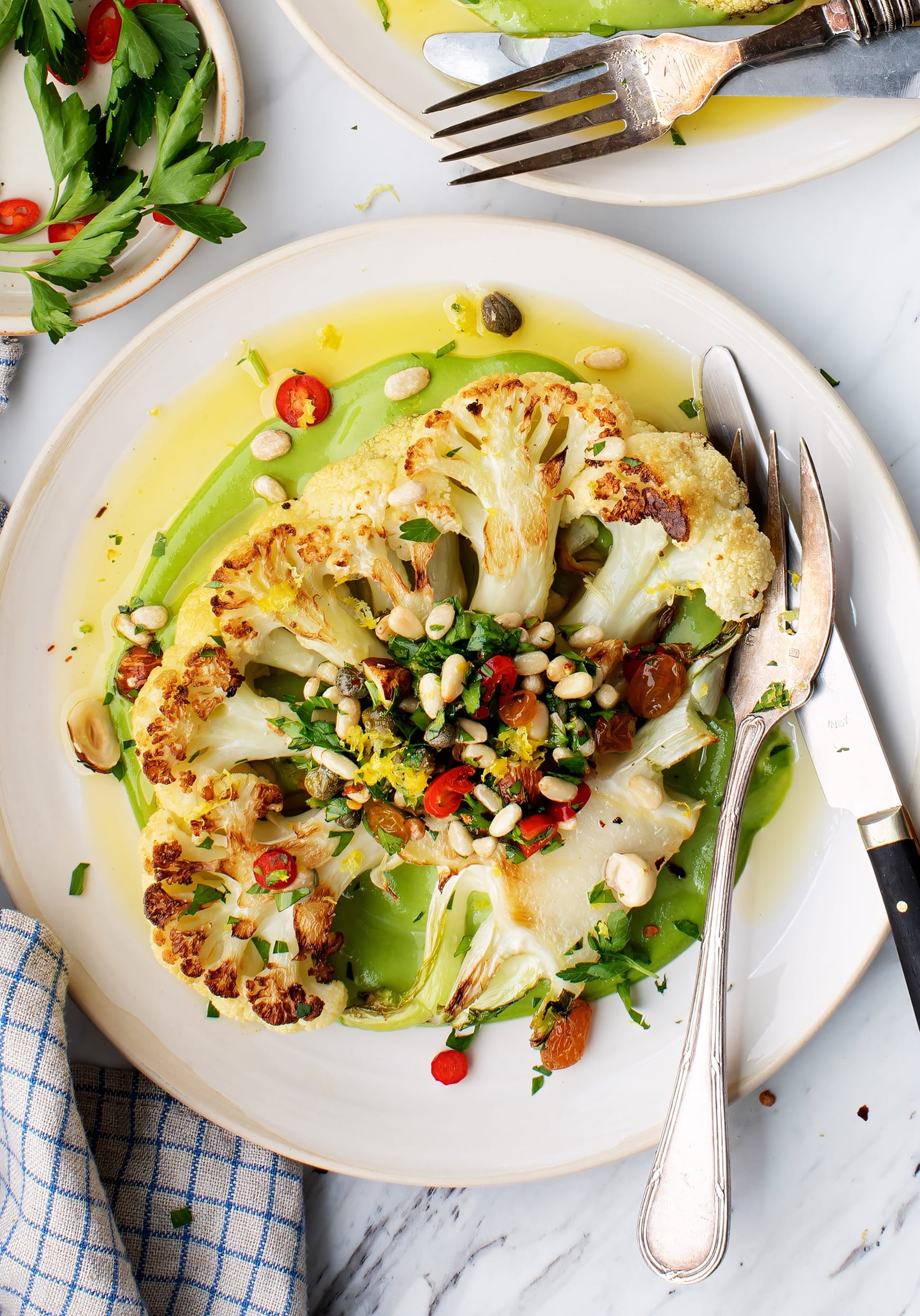 A beautifully roasted cauliflower steak alongside vibrant broccoli florets, garnished with fresh herbs.
