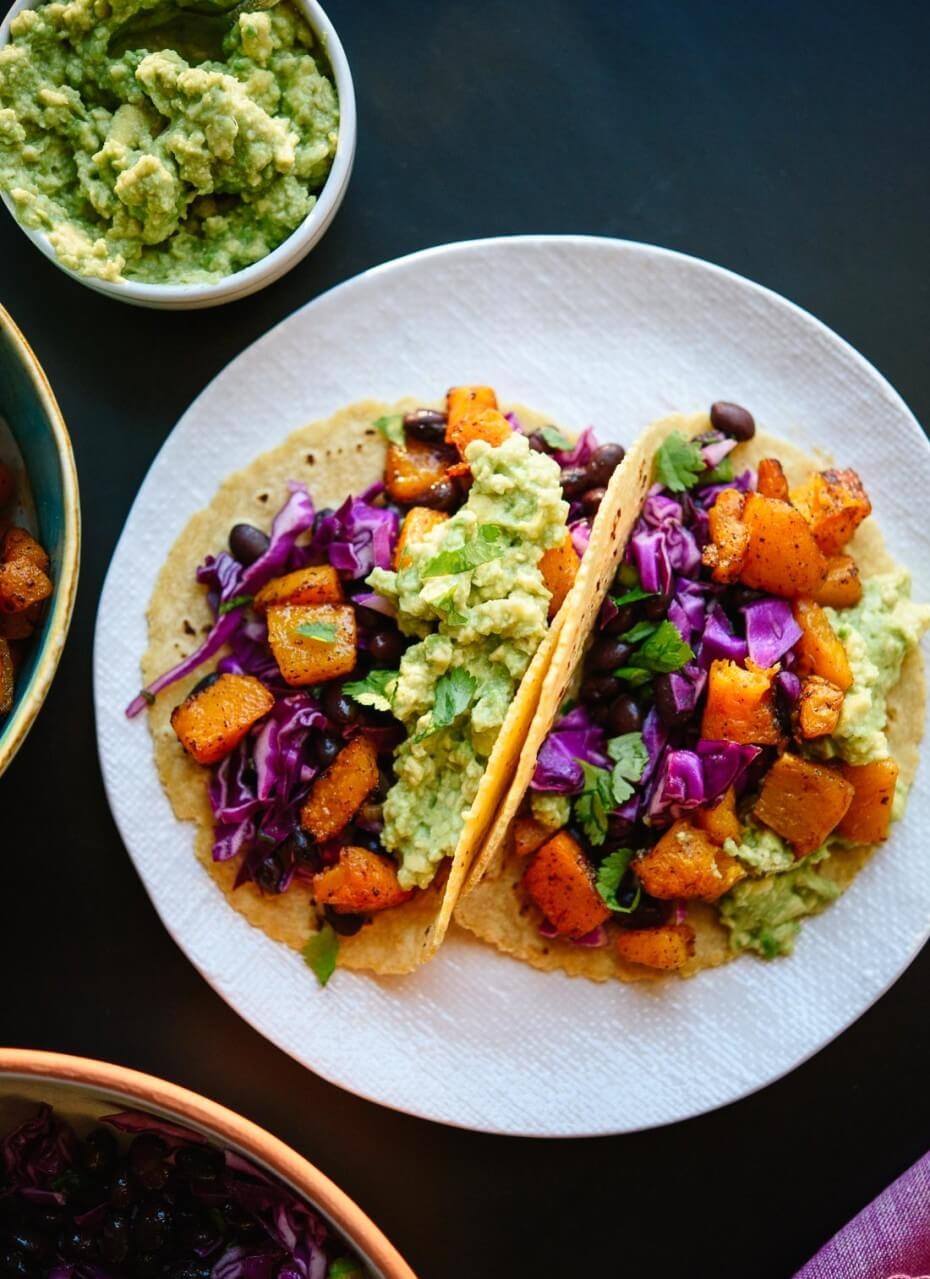 Butternut squash tacos with sage garnish on a rustic wooden table