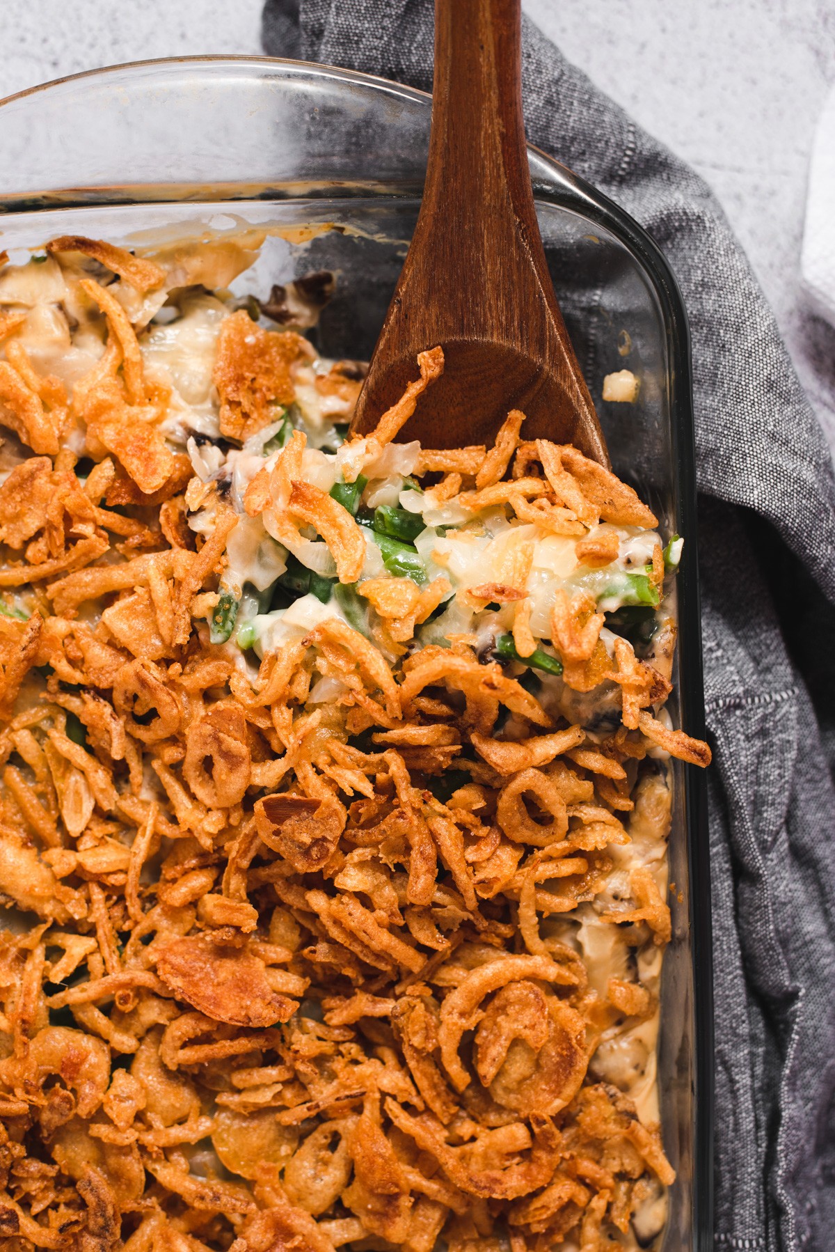 Homemade green bean casserole with golden crispy fried onions on top, a cozy kitchen setting