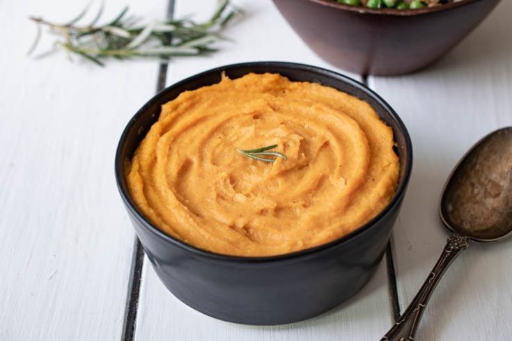 Close-up shot of a bowl of creamy roasted carrot and parsnip puree, garnished with fresh herbs