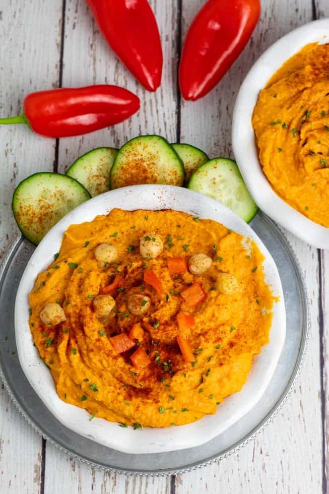 Vibrant red pepper hummus in a bowl with pita bread and vegetables, overhead shot