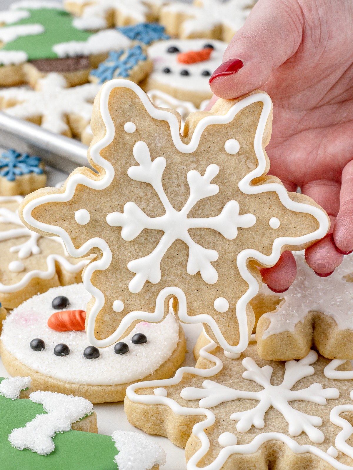 beautifully decorated vanilla sugar cookies with intricate hand piped designs, some stacked on a plate, warm inviting light