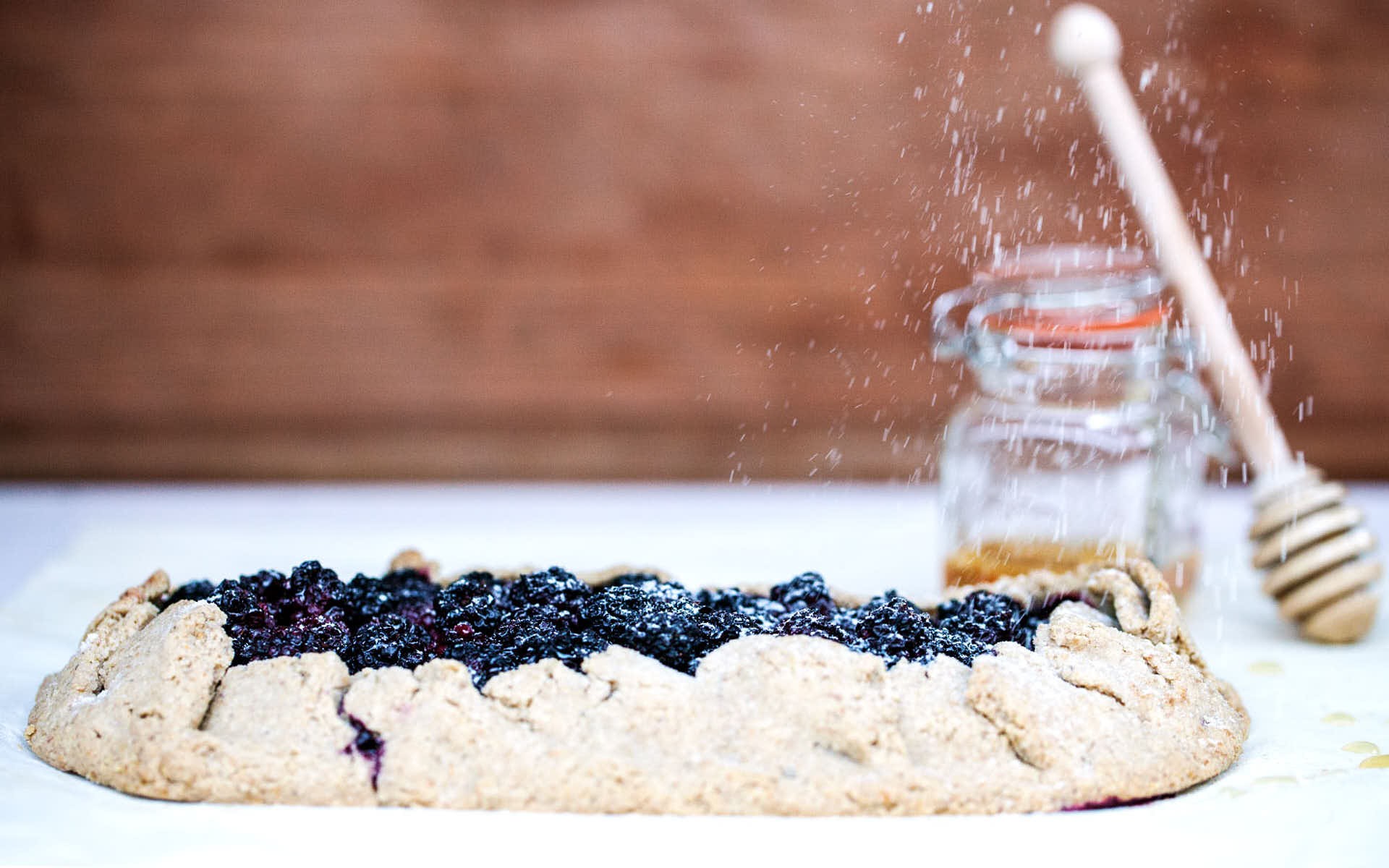 A rustic blackberry thyme tart on a white linen tablecloth with fresh blackberries and thyme sprigs scattered around