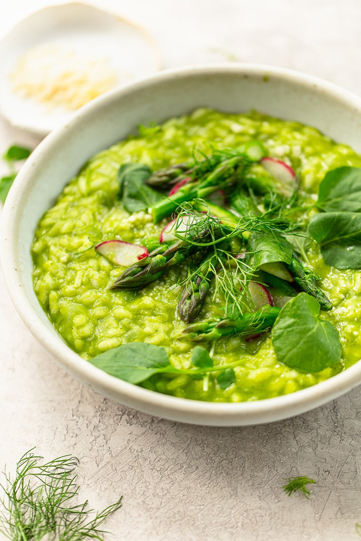A vibrant, creamy risotto with bright green asparagus spears and thin slices of radish, garnished with fresh dill