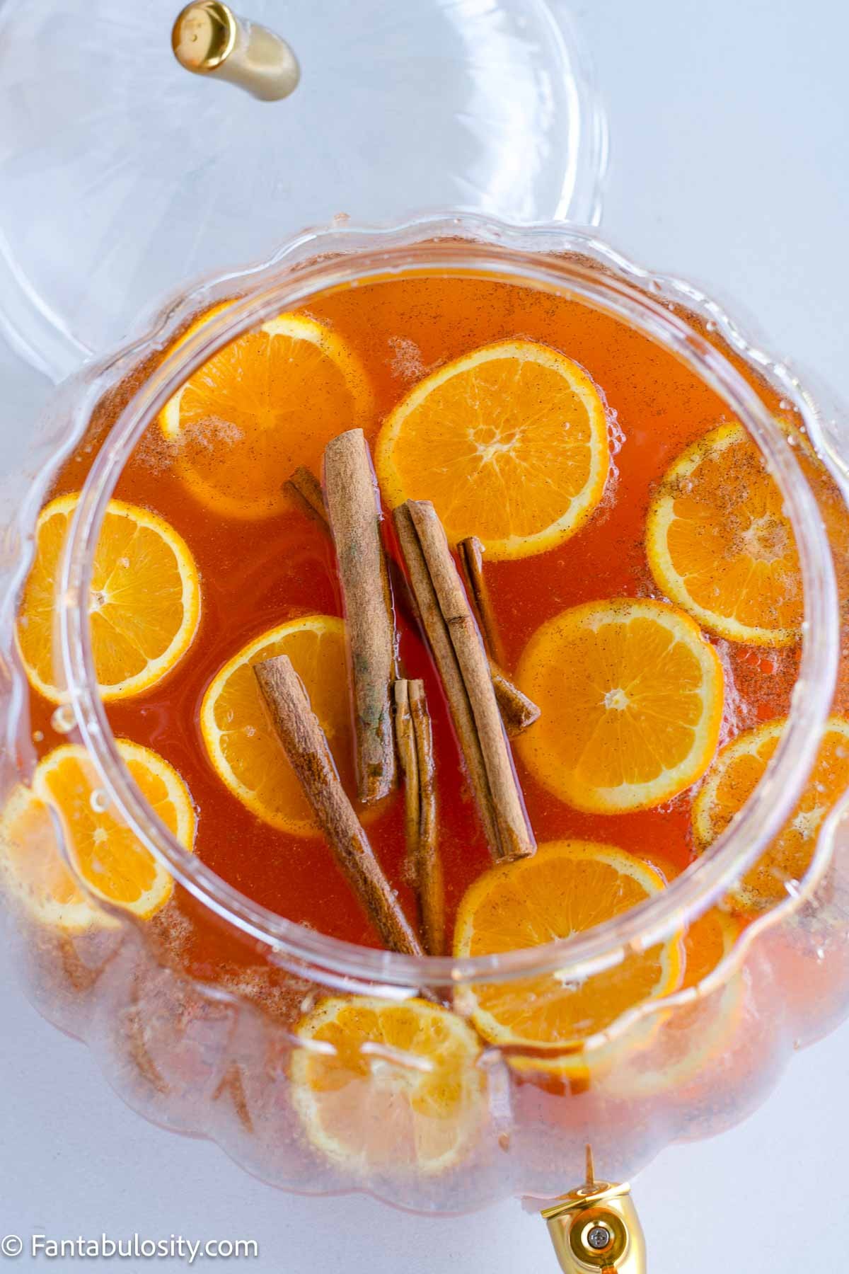 Vibrant Friendsgiving caramel apple punch in a large glass dispenser with apple slices and cinnamon sticks, surrounded by autumn decor and smiling friends clinking glasses