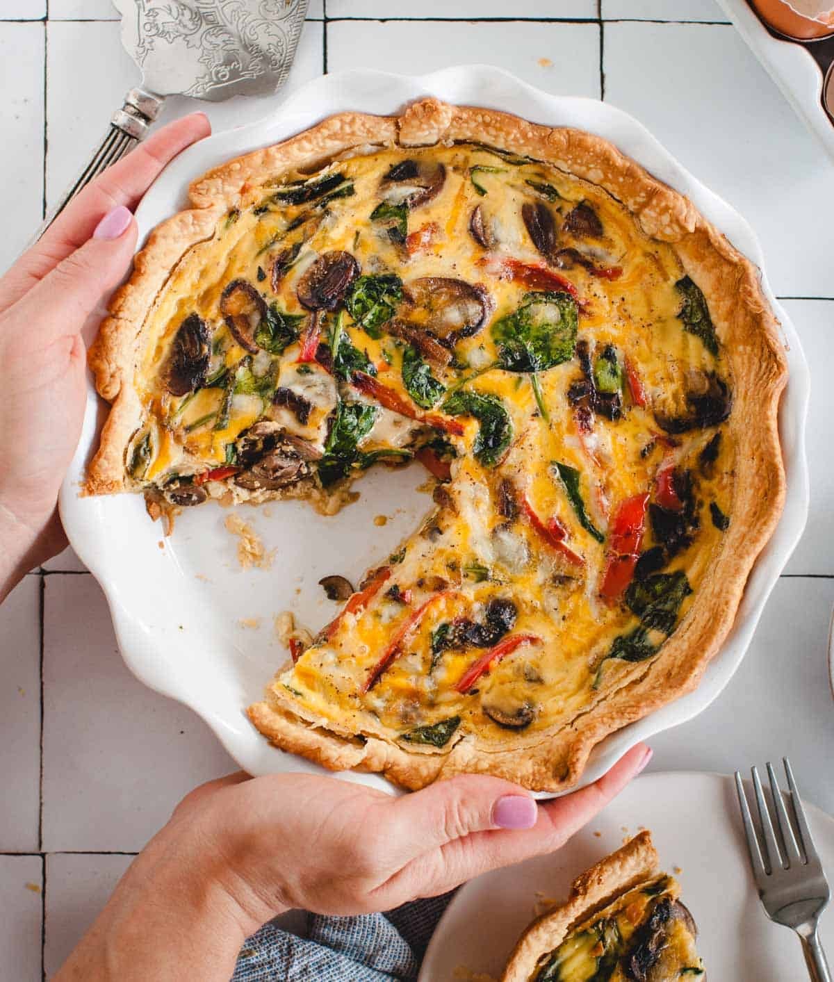 A rustic looking, golden-brown grilled vegetable quiche sliced and served on a white plate with fresh herbs