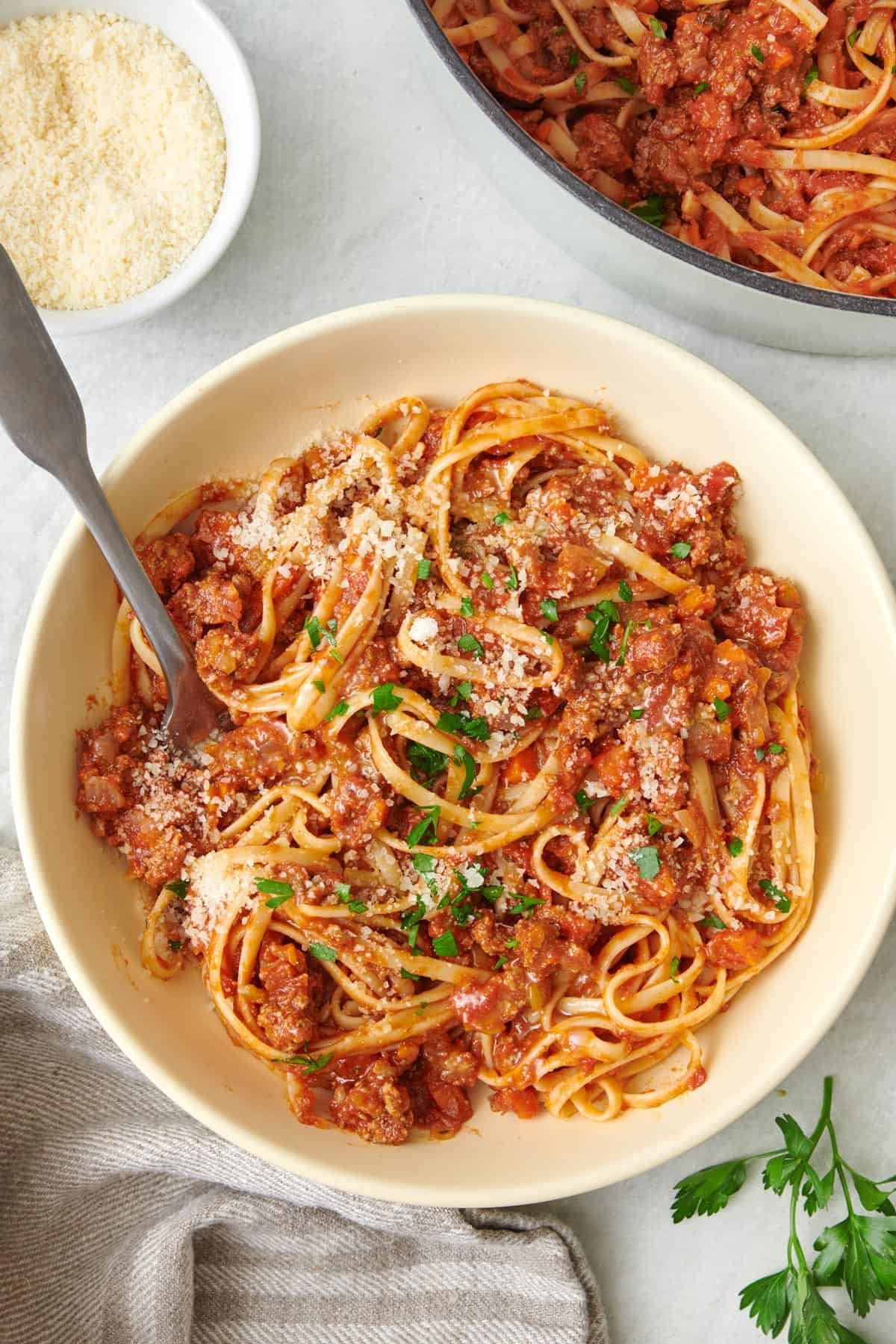 a close-up shot of a bowl of beef bolognese served over pasta, garnished with fresh basil and Parmesan cheese