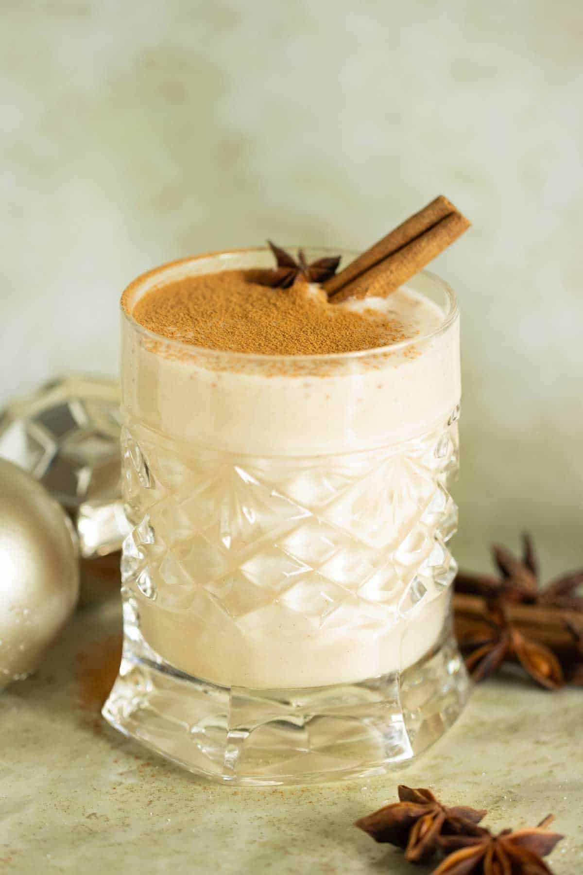 A beautifully garnished glass of coquito, rich and creamy, with a cinnamon stick and star anise, surrounded by festive holiday decorations