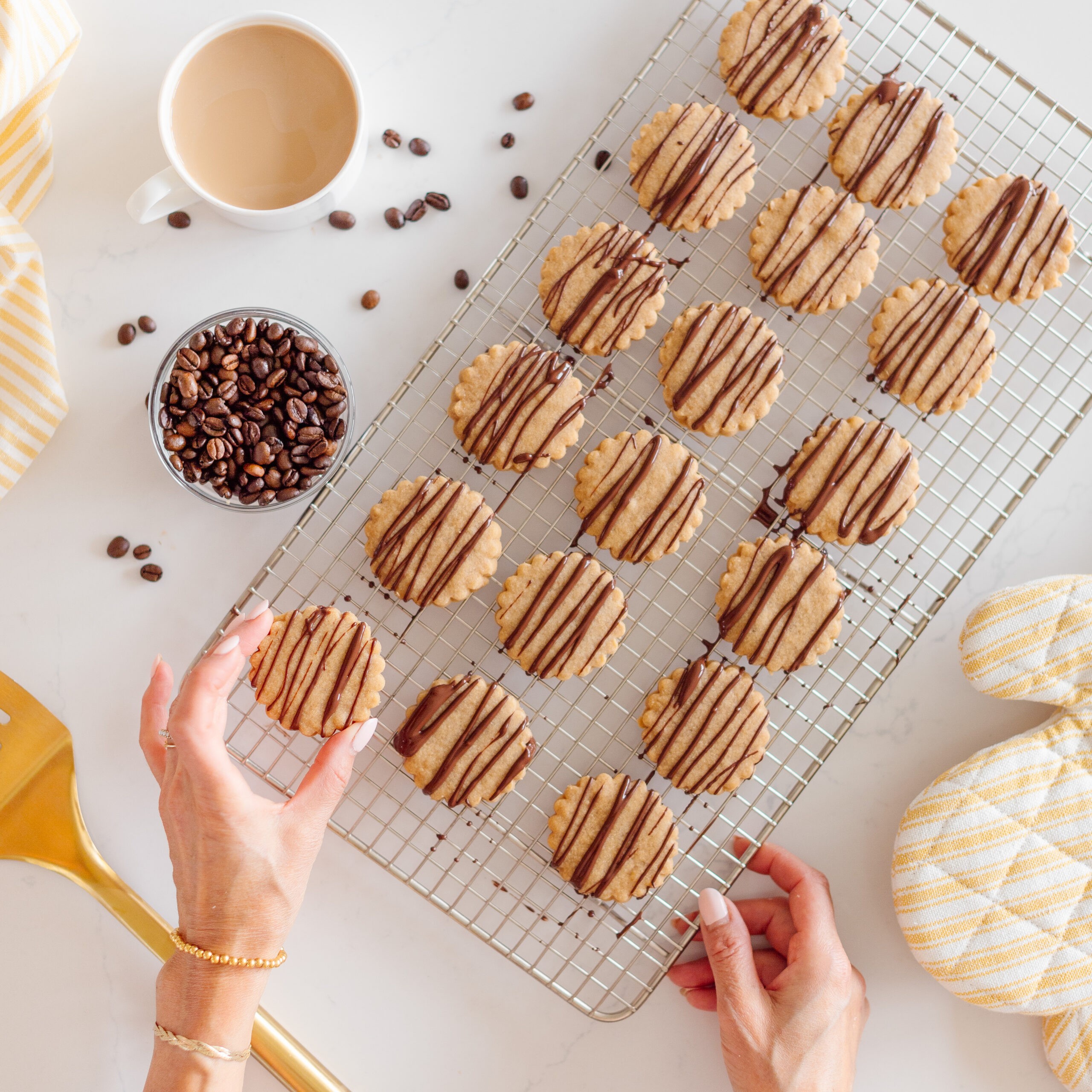 Close-up of golden brown espresso shortbread cookies on a cooling rack, some with a dusting of cocoa powder, a cup of coffee in the background, warm lighting