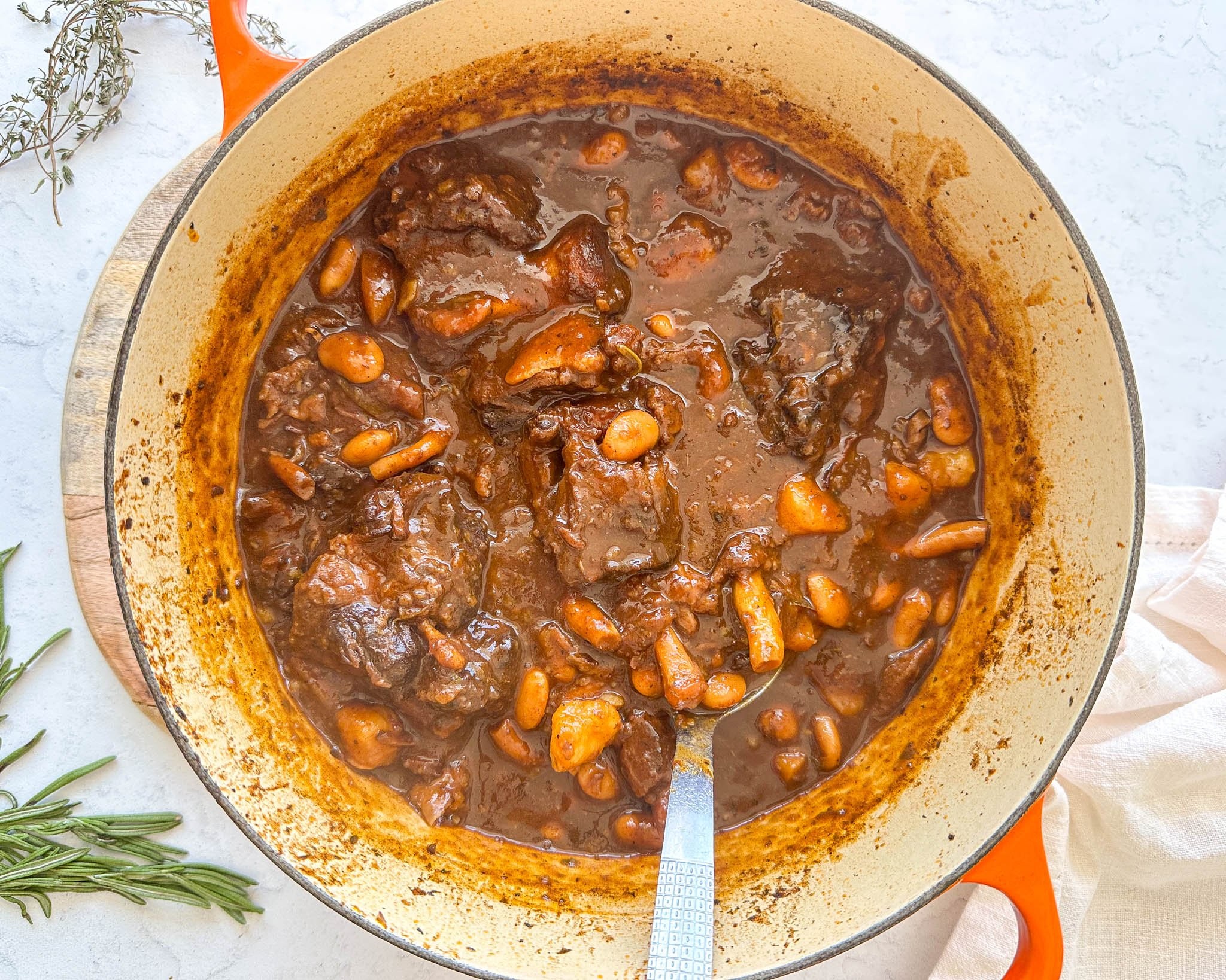 a pot of orange oxtail stew simmering on a stove, garnished with fresh orange zest and parsley