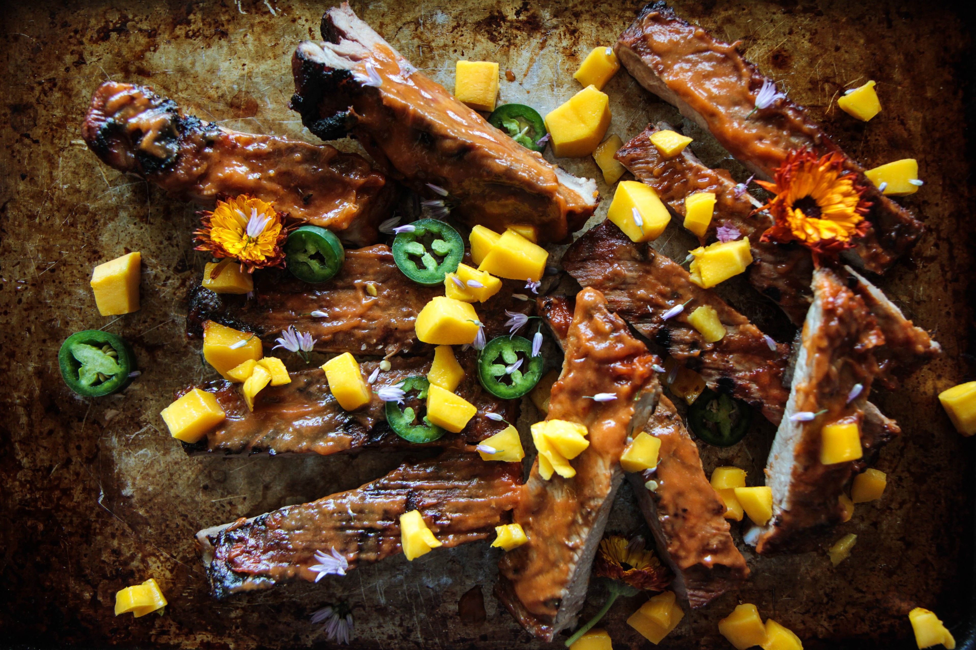 spicy mango BBQ ribs on a wooden cutting board with mango slices and herbs