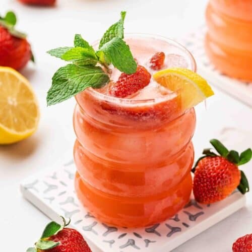 vibrant non-alcoholic strawberry lemonade fizz in elegant glass, garnished with fresh mint and strawberries, holiday backdrop