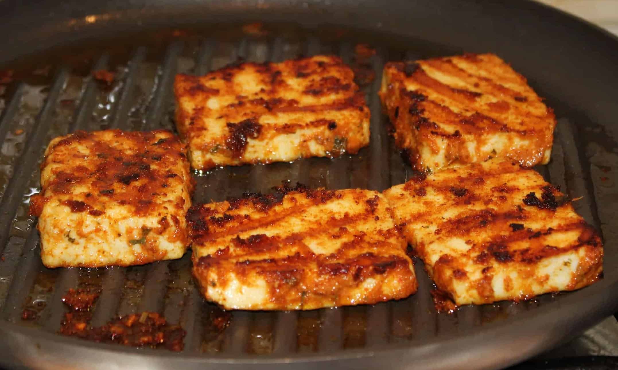 Close-up shot of flavorful paneer tikka cubes with a sprinkle of cinnamon on a grill pan