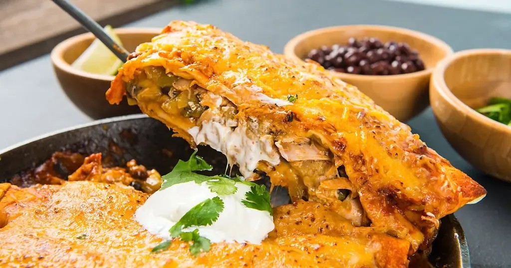 Close-up shot of golden-brown roasted chicken enchiladas in a baking dish, garnished with fresh cilantro