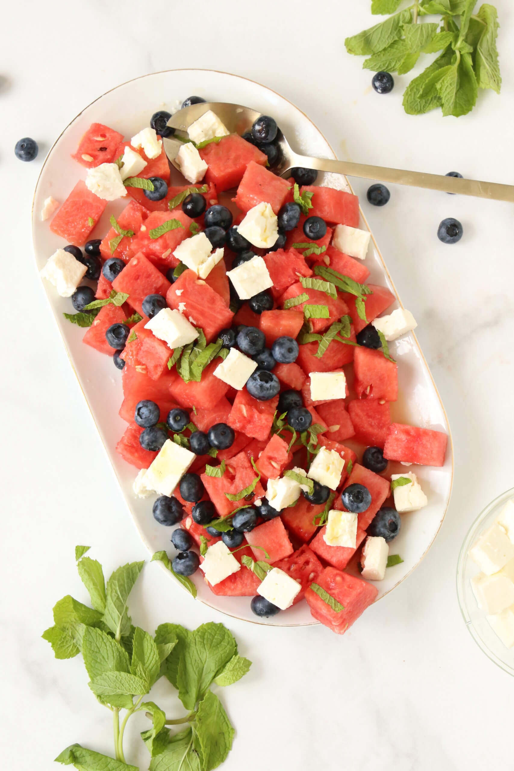 A vibrant watermelon salad with blueberries and lemon zest, garnished with fresh mint.