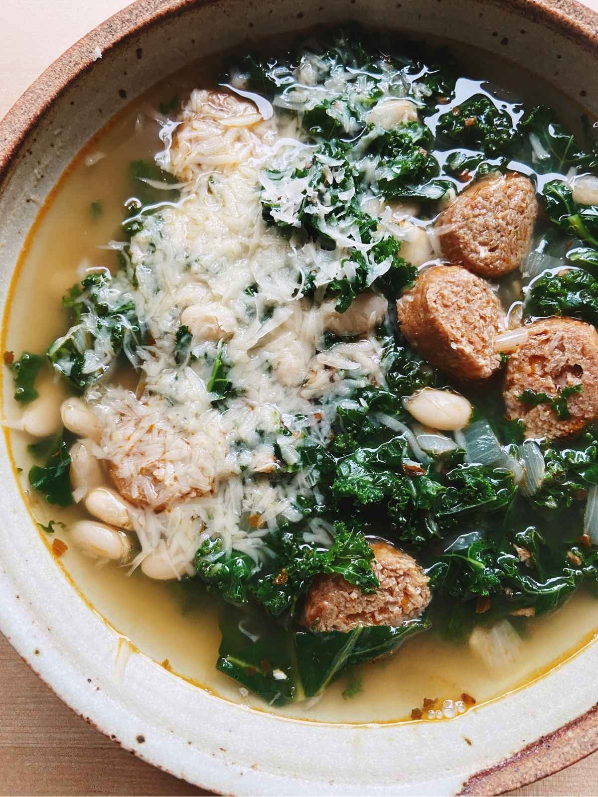 A rustic bowl of hearty kale and white bean soup with sausage, garnished with fresh parsley