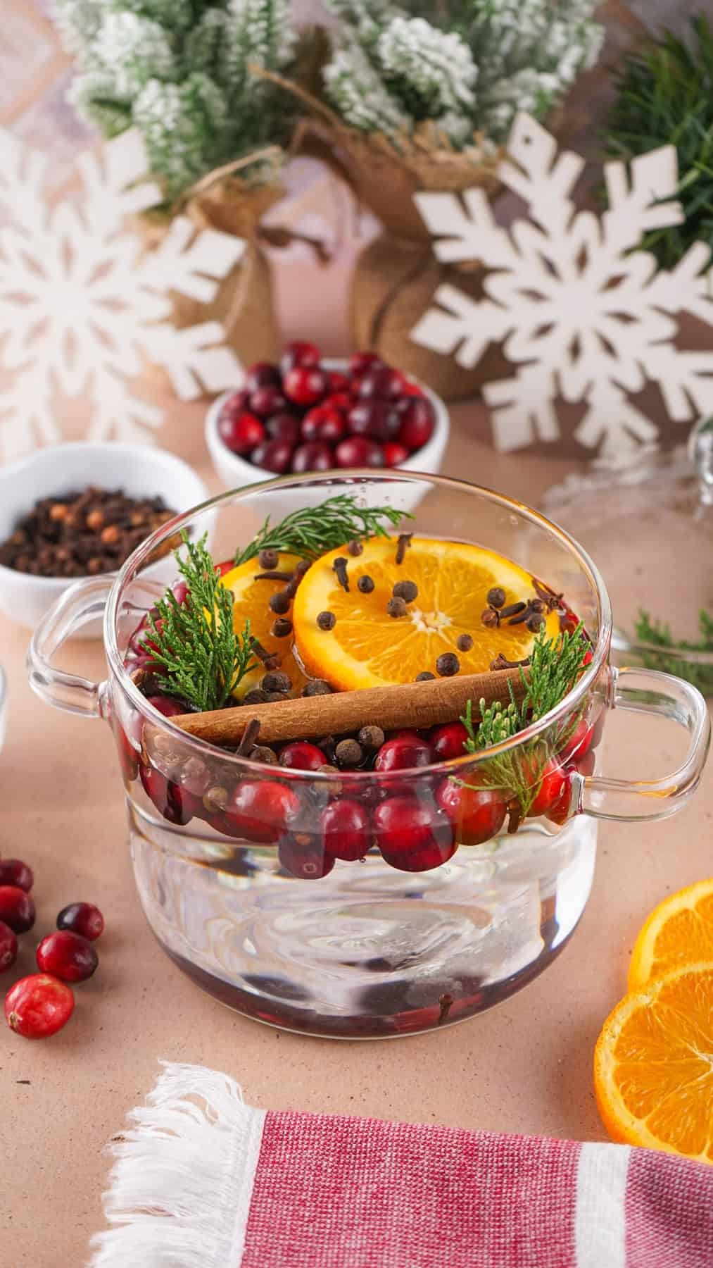 Cozy Christmas kitchen with a steaming mug of spiced apple drink, a decorative simmer pot with fruit and spices, warm fairy lights