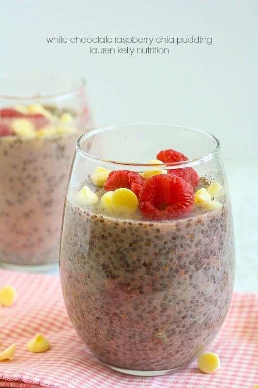 Close-up shot of white chocolate raspberry chia pudding in glass jars, garnished with fresh raspberries and white chocolate shavings.