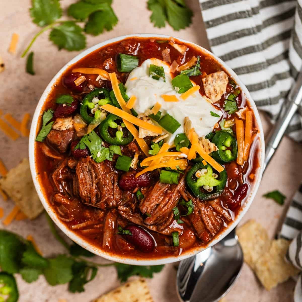 Close up of tender, shredded chili beef roast with visible steam, garnished with cilantro in a rustic bowl
