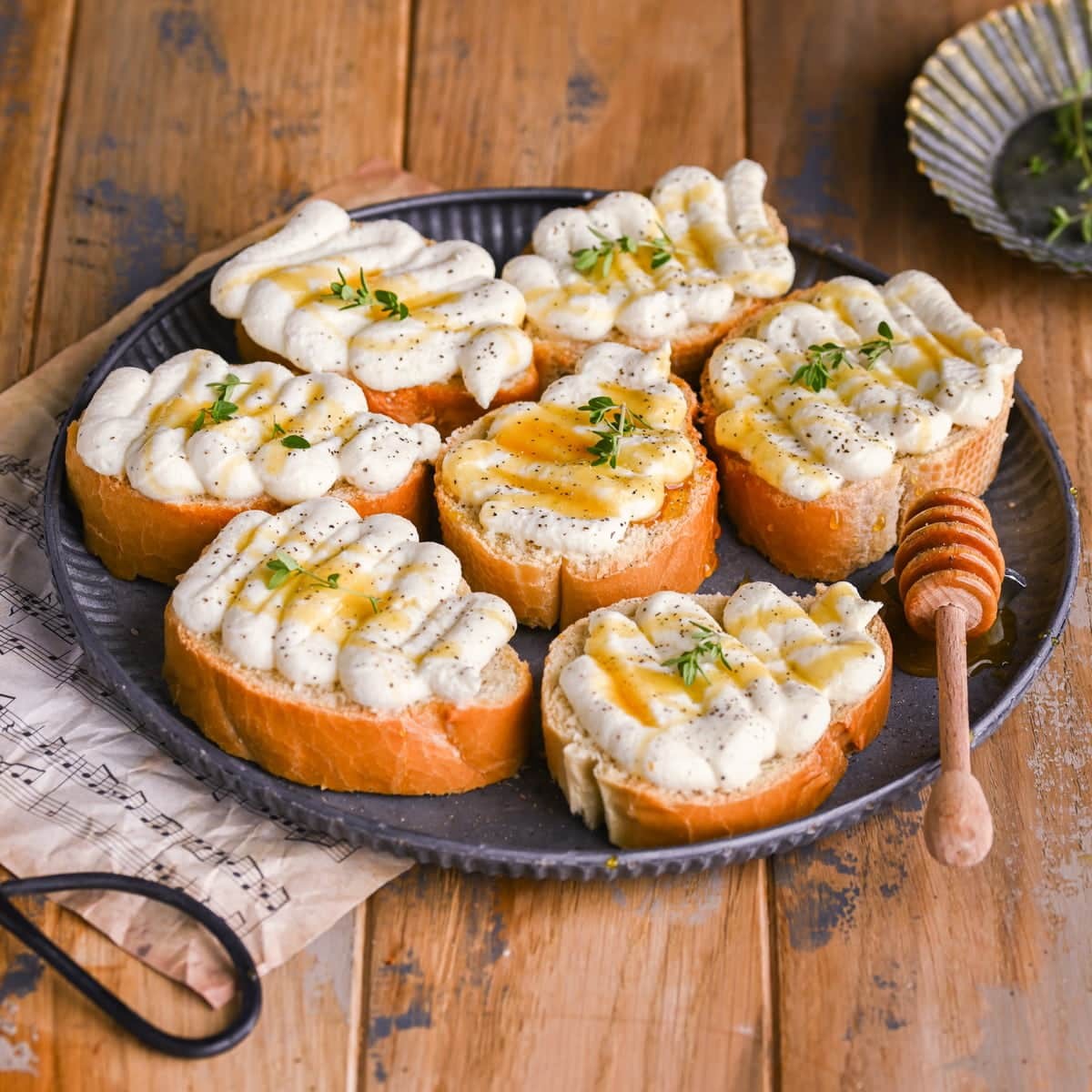 crispy crostini with creamy whipped ricotta and fresh herbs, close-up, rustic wooden board
