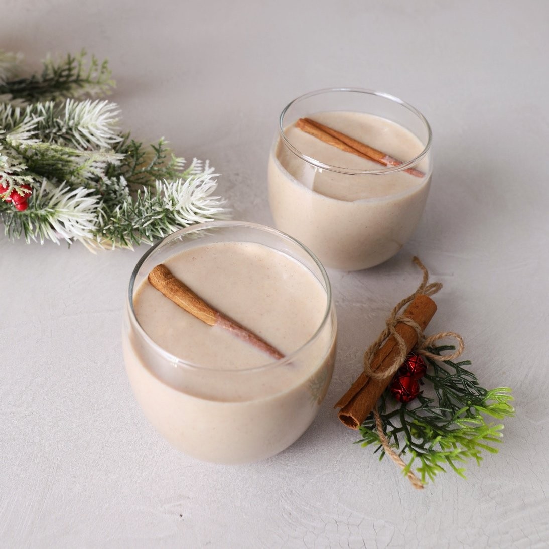 Festive Coquito drink with cinnamon sticks and nutmeg, holiday decorations in background