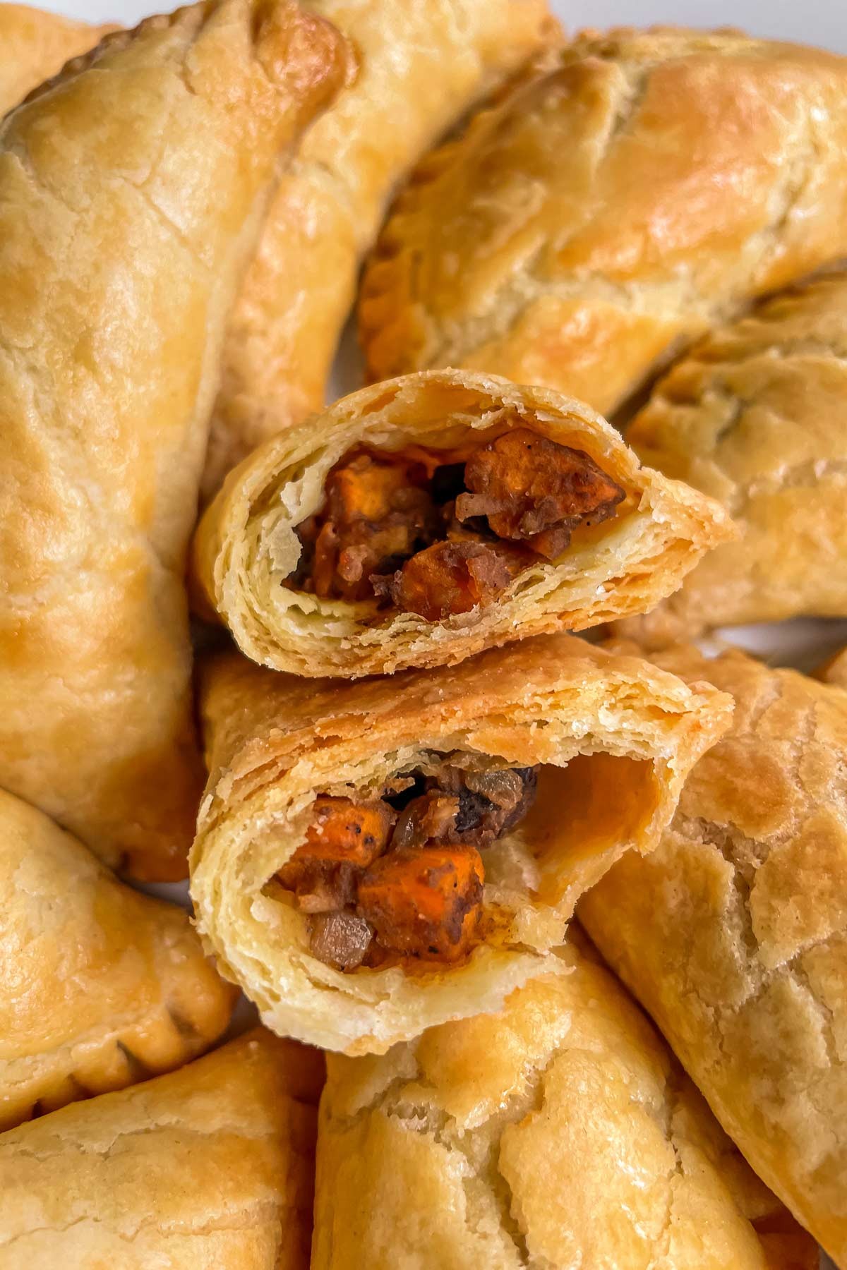 Close-up shot of golden-brown sweet potato and black bean empanadas drizzled with spicy peanut sauce