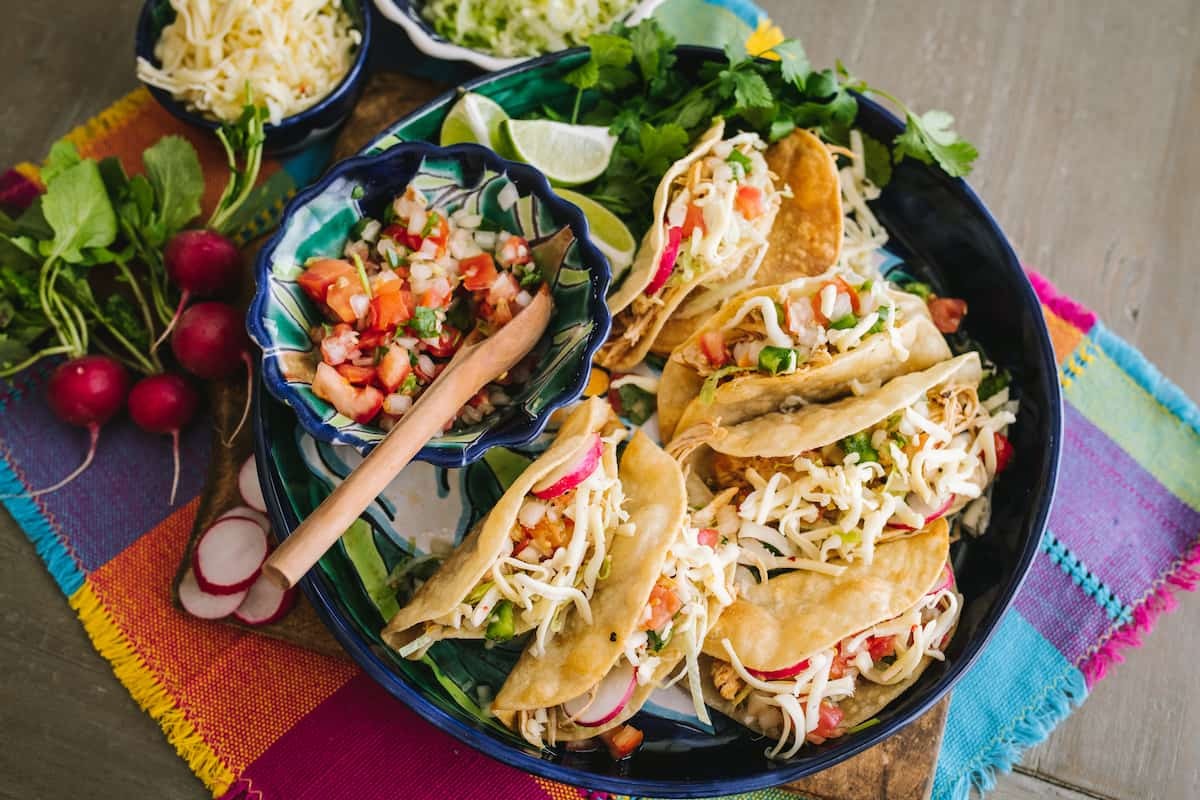 overhead shot of colorful chicken taco wraps on a wooden board with various toppings