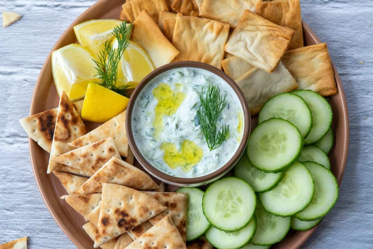 bowl of tzatziki sauce with pita bread and cucumber slices