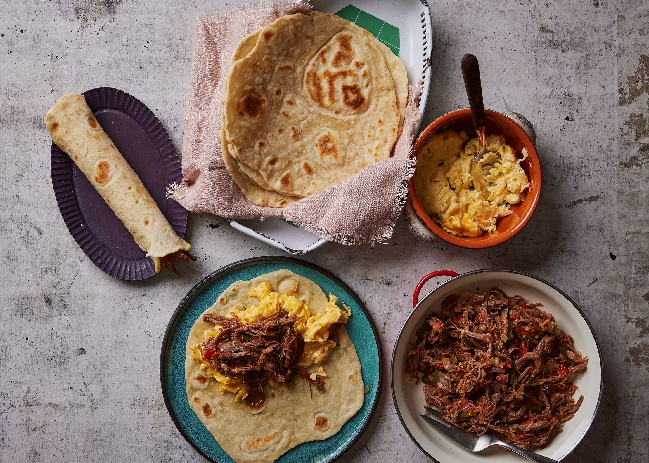 A rustic wooden table setting featuring a golden-brown Tortilla Española alongside a small bowl of creamy tartar sauce.