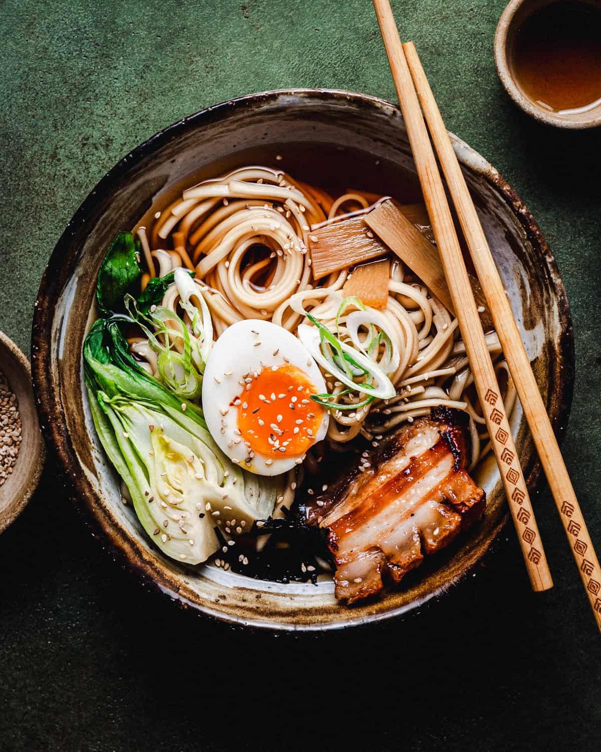 A steaming bowl of ramen with chashu pork, garnished with scallions and nori.