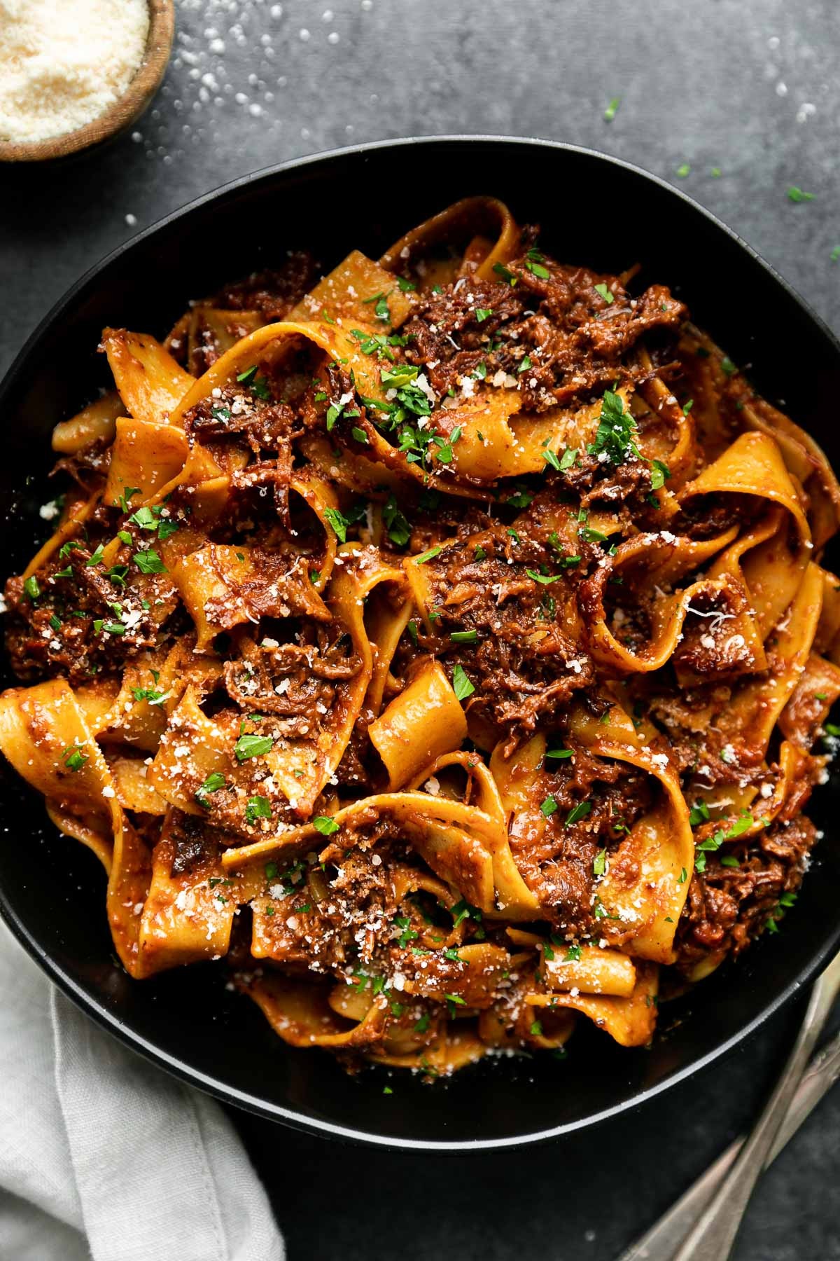 Close-up shot of tender short rib ragu served over pappardelle pasta with a sprinkle of vibrant gremolata