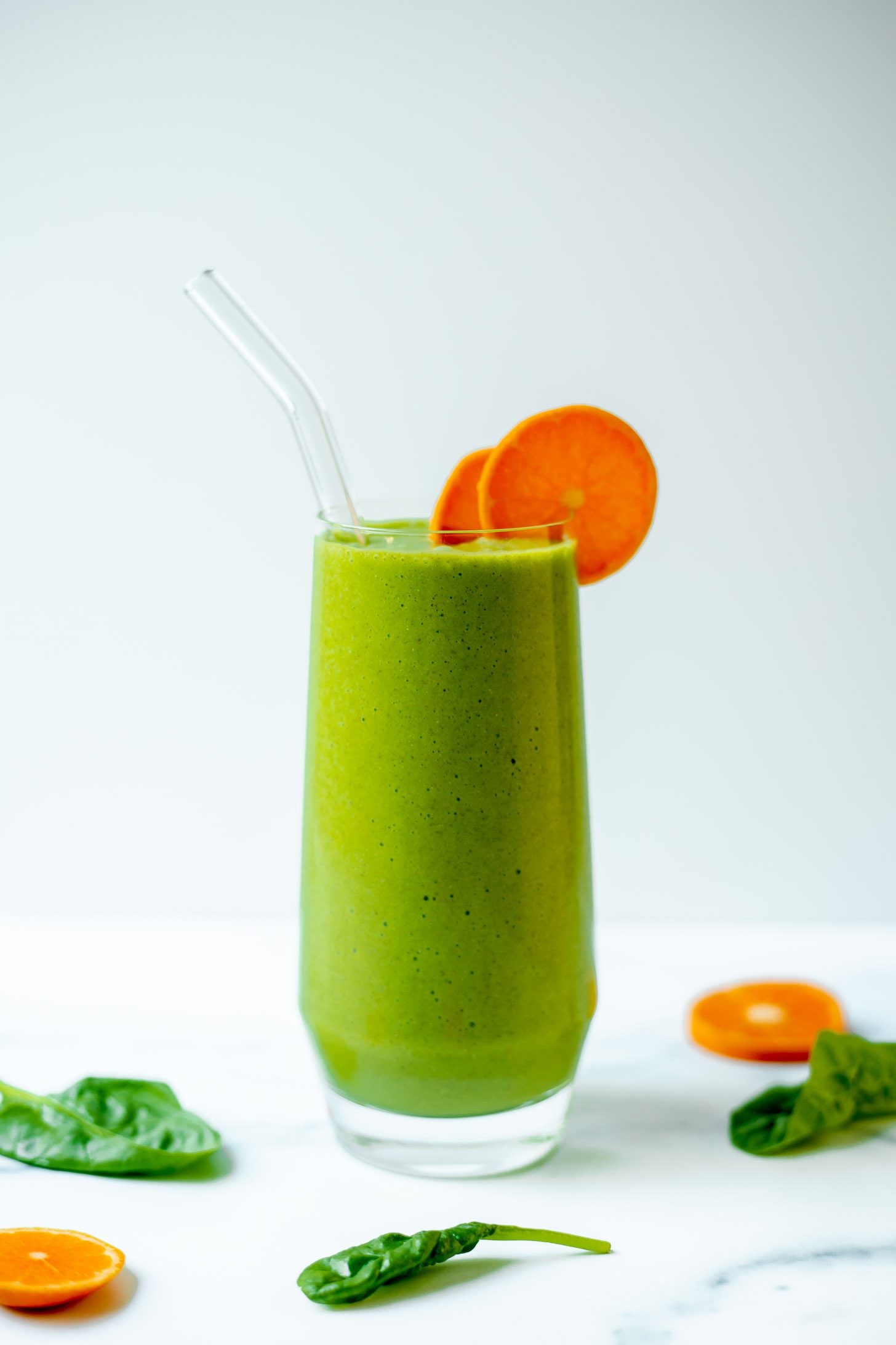 vibrant green vegan smoothie in a glass with fresh ingredients around it