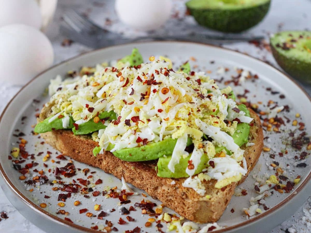gourmet avocado egg toast with runny yolk and chili flakes on rustic bread