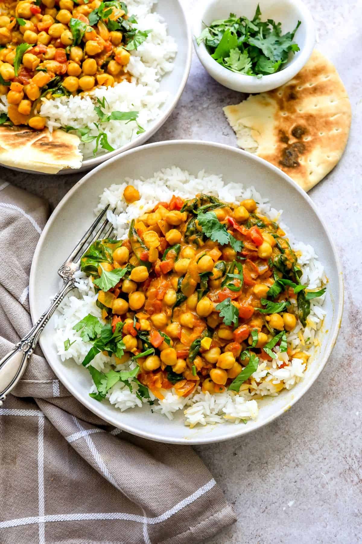 Vibrant chickpea spinach curry in a rustic bowl, garnished with fresh cilantro, with naan bread on the side