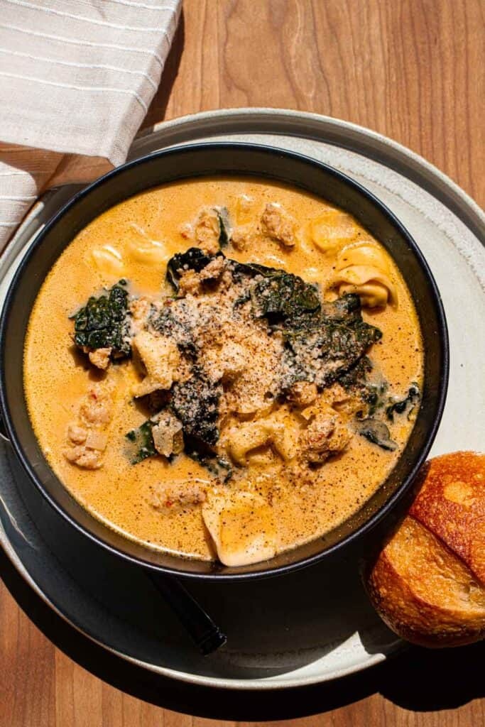 A rustic bowl of pumpkin soup with Italian sausage and kale, garnished with a swirl of cream and a sprinkle of parmesan cheese.