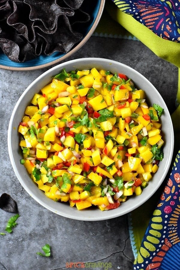 A vibrant bowl of mango salsa with fresh cilantro and red onion, garnished with lime wedges