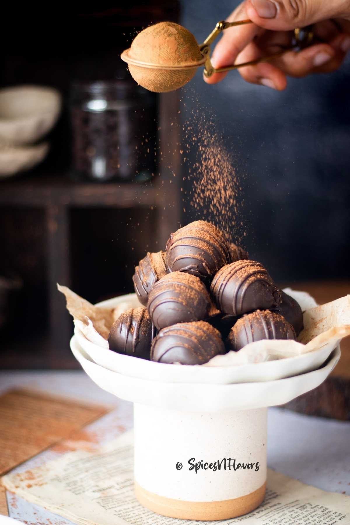 Hand dusting espresso truffles with cocoa powder on a rustic wooden board, elegant lighting.
