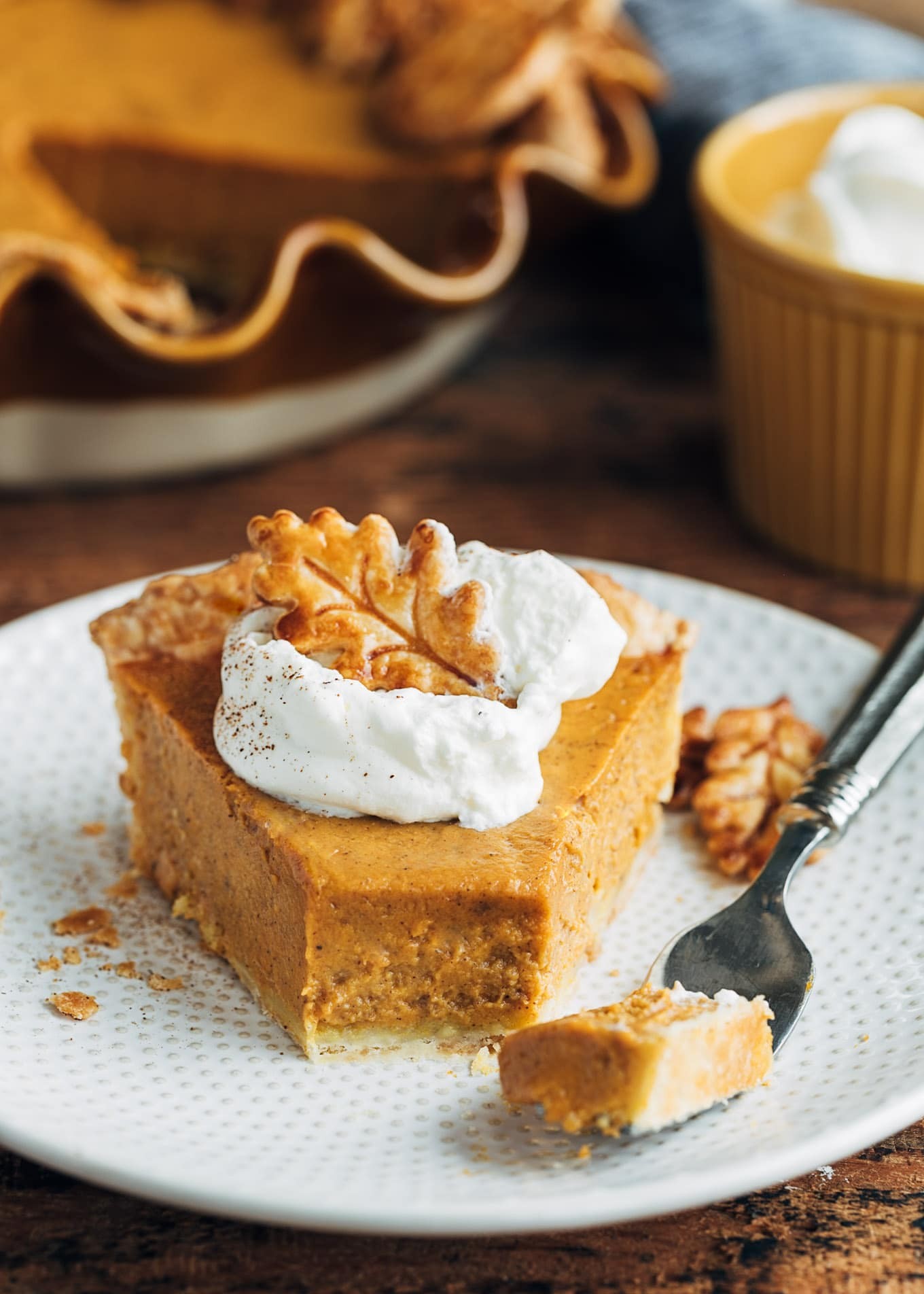 beautifully baked classic pumpkin pie with smooth custard filling, garnished with whipped cream, on a rustic wooden table with autumn leaves