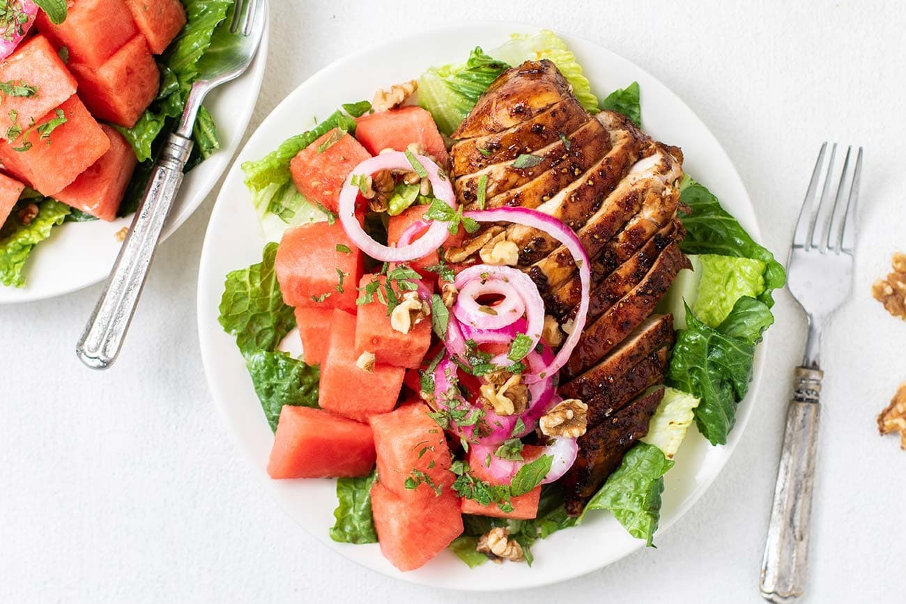 A vibrant watermelon salad with grilled chicken and mango, garnished with fresh mint