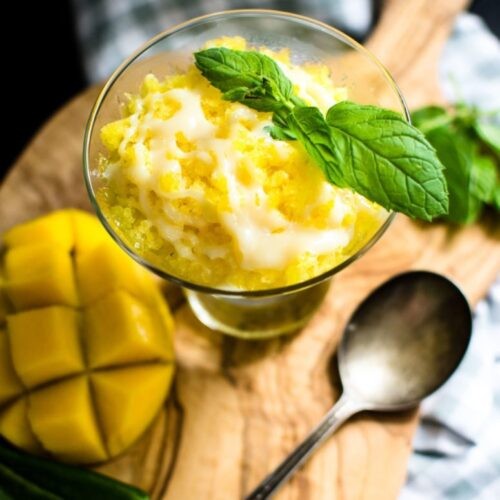 Close-up shot of mango chili kombucha granita in a glass, with fresh mango slices and chilies in the background