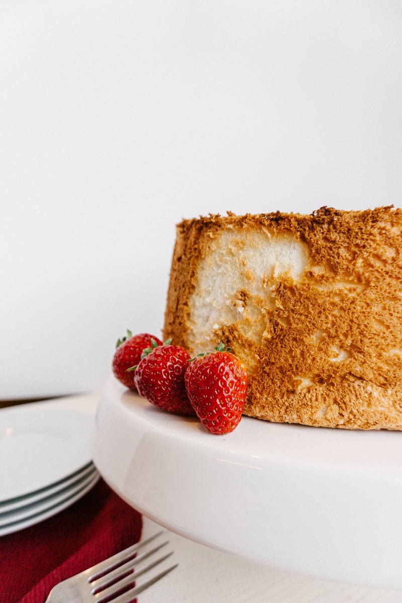 A perfectly baked, light and airy angel food cake, dusted with powdered sugar, sitting on a wire rack
