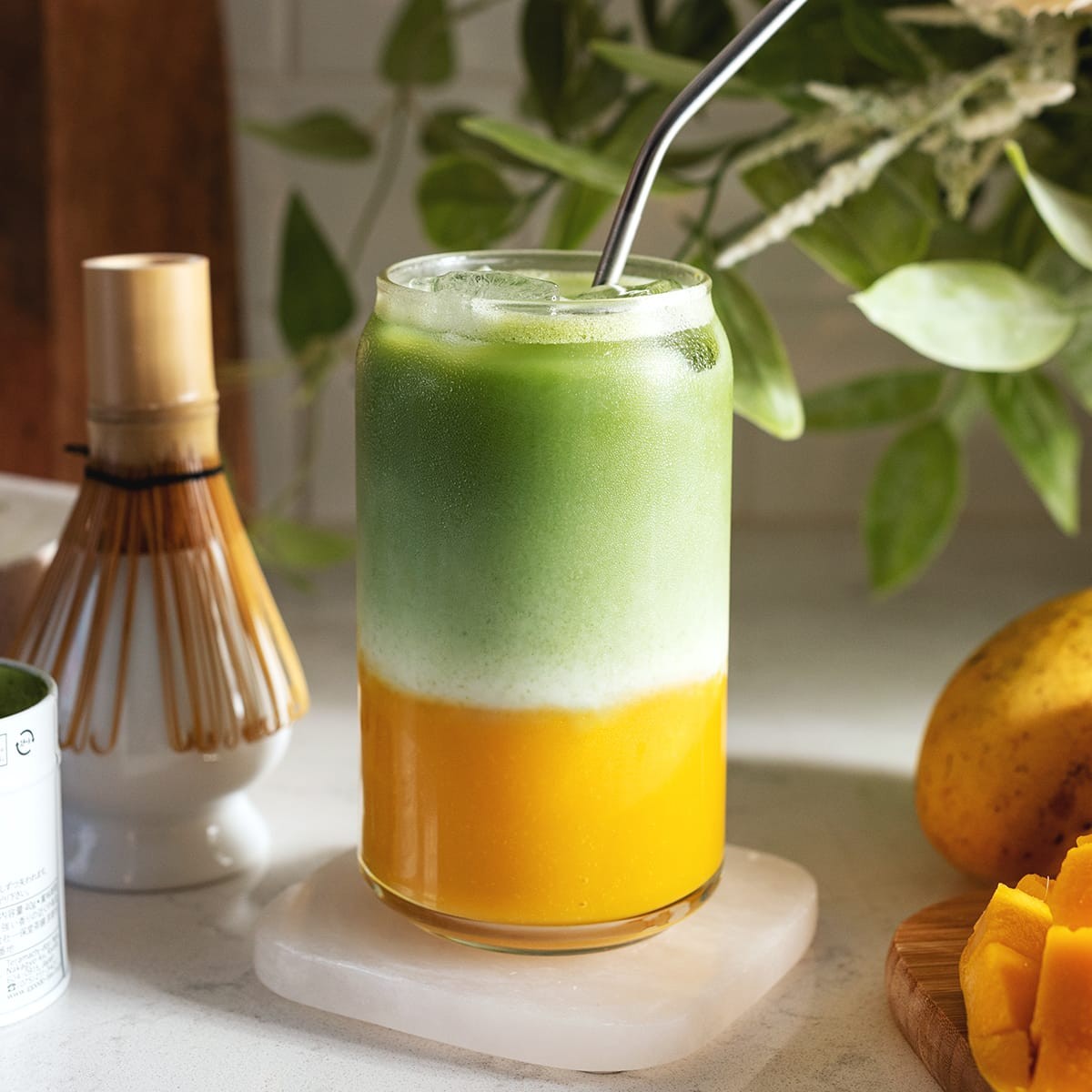 vibrant green matcha mango smoothie in a glass with ice and mango slices