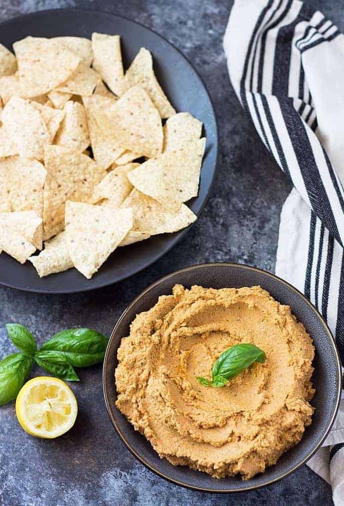 sun-dried tomato basil hummus in a bowl with pita bread and fresh basil