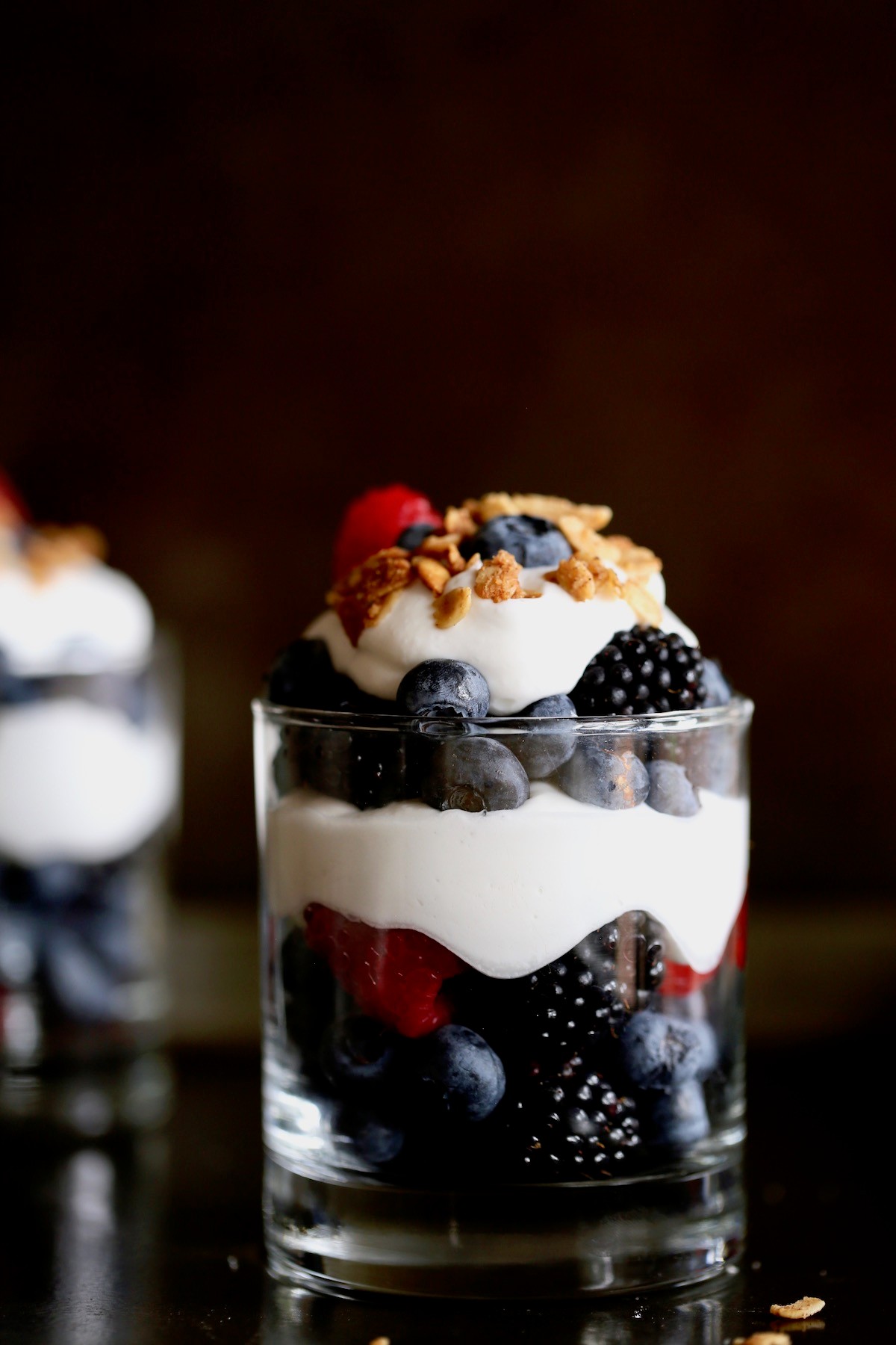 A vibrant berry parfait smoothie in a tall glass with fresh berries and granola on top.