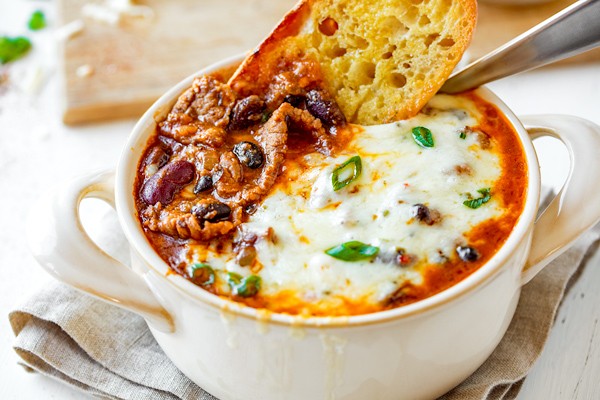 steaming bowl of rustic beef chili stew with crusty bread and a cozy background