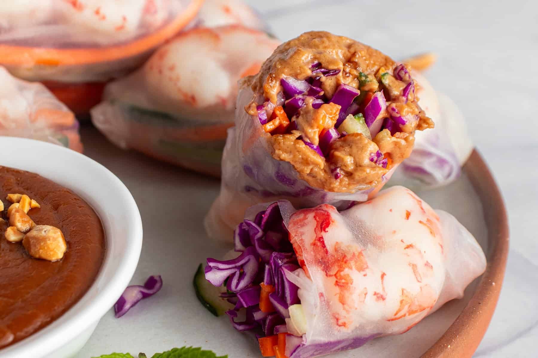 Close-up shot of vibrant, colorful edamame and shrimp spring rolls arranged on a rustic wooden board with a dipping sauce on the side.
