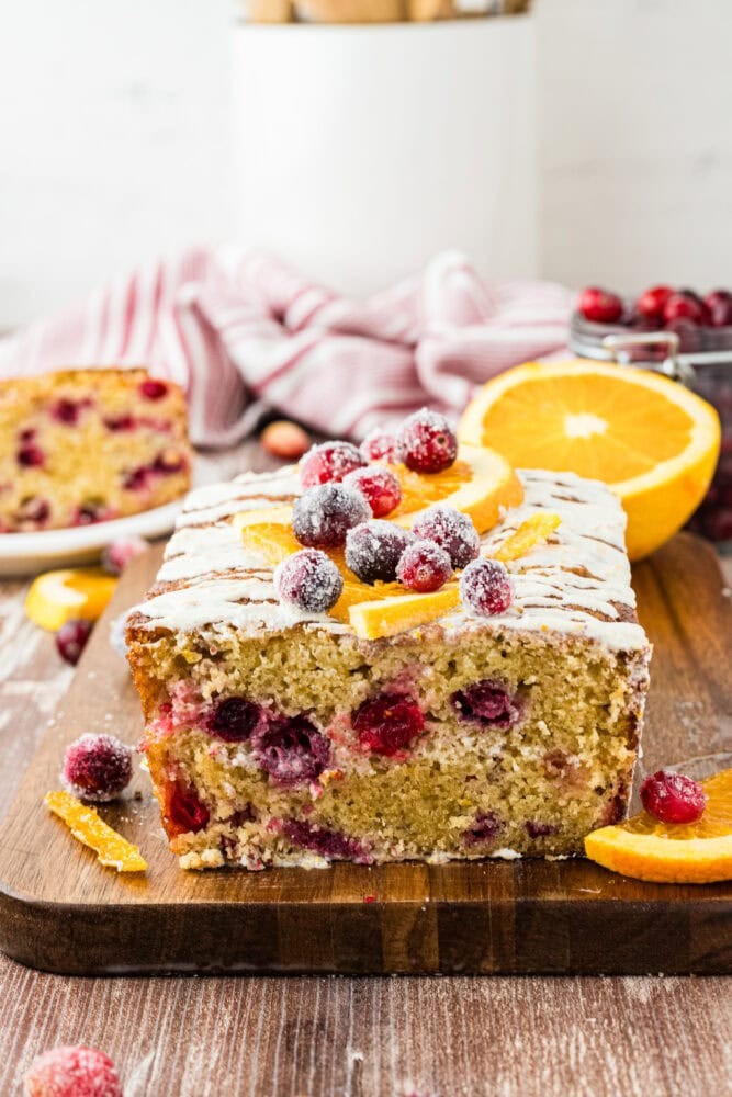 Vibrant cranberry orange bread, sliced on a wooden board, with fresh oranges and cranberries