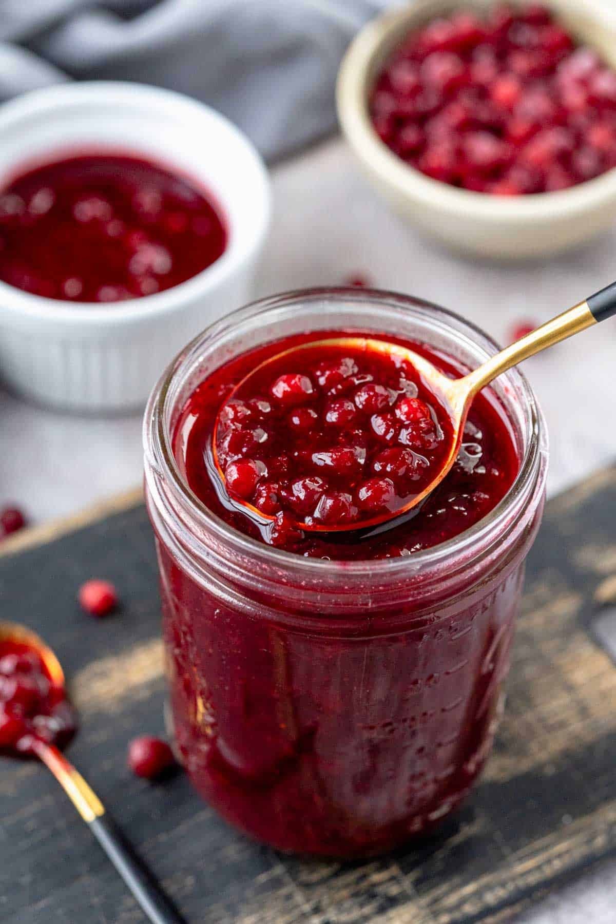 A jar of homemade lingonberry jam next to a bowl of cranberry sauce