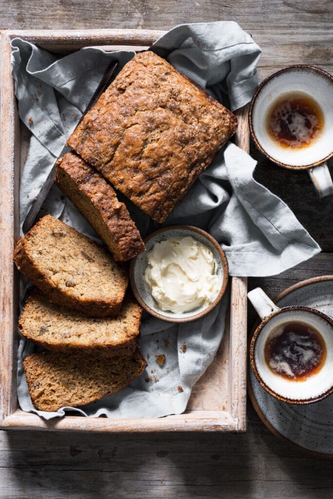 Warm, rustic browned butter banana bread loaf, sliced, with a cup of coffee on a wooden table, cozy setting