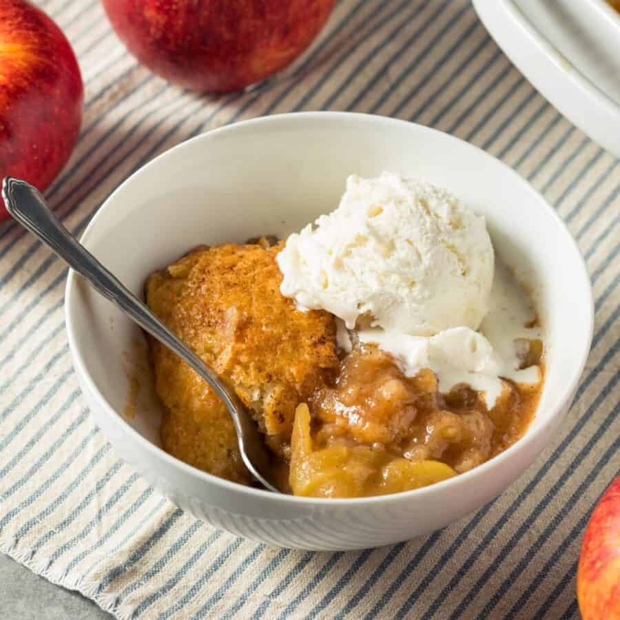A rustic, golden-brown apple crisp cobbler in a baking dish, garnished with a scoop of vanilla ice cream